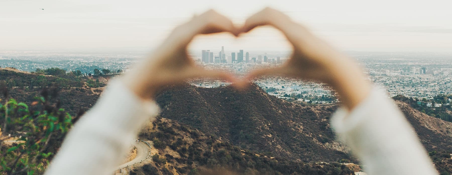 lifestyle image of hands making a heart shape with the distant city in the background